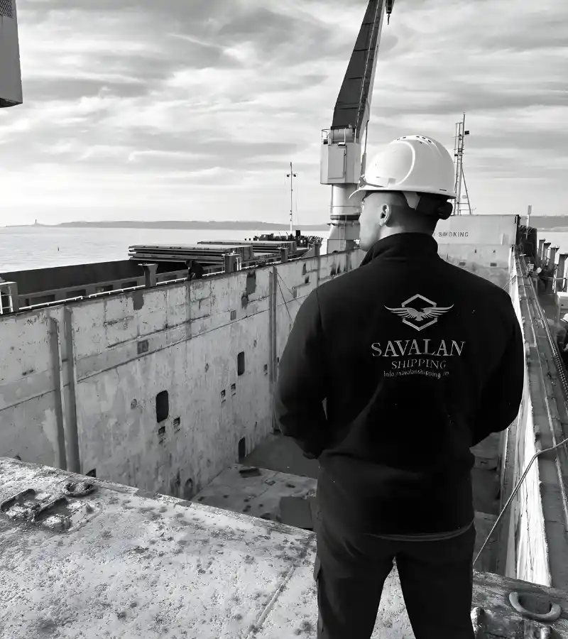 A Savalan Shipping team member in a hard hat standing on a vessel deck, overlooking the cargo area and the sea.